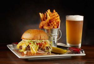 Burger and fries meal with pickle, ketchup, and beer on the side at Cafe Hollywood